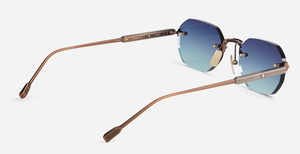 Randlose Sonnenbrille mit blau-türkisem Glasverlauf und schlanken bronzefarbenen Metallbügeln in seitlicher Rückansicht.“