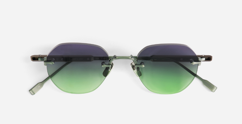 Nahaufnahme der randlosen Sonnenbrille mit violett-grün getönten Gläsern, sichtbaren Metallbügeln und filigranem Nasensteg